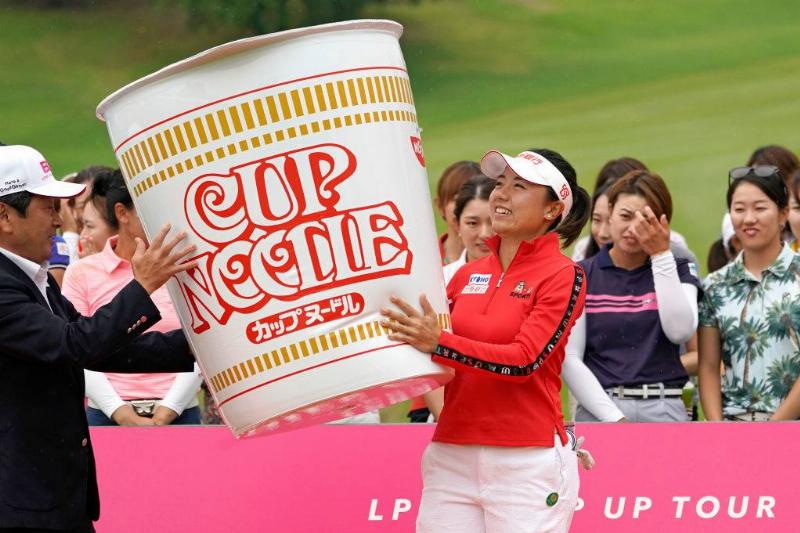a golfer holding a giant Cup Noodle