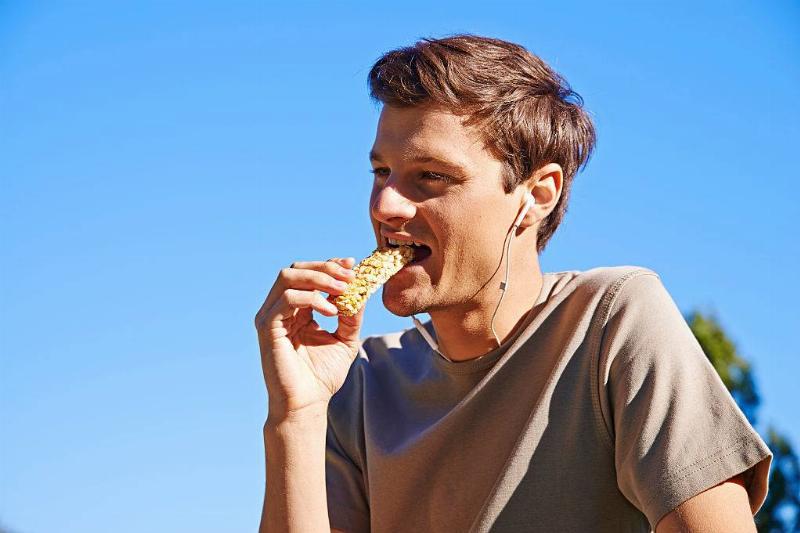 a teen boy eating an energy bar and wearing earbuds