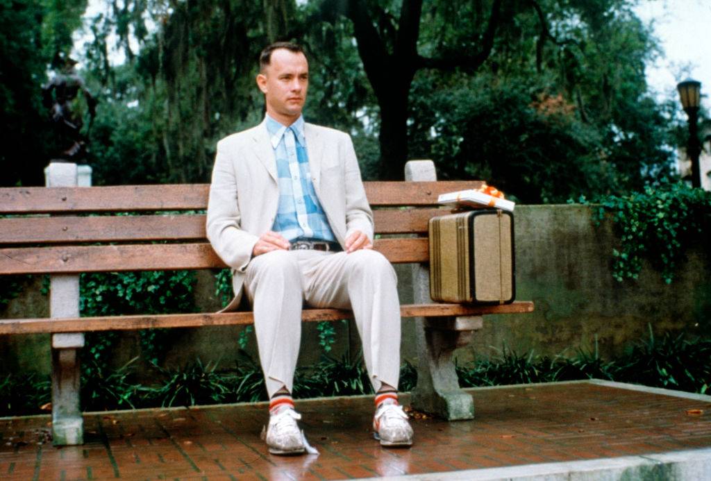 tom hanks sitting on a bench in forrest gump with a suitcase and a box of chocolates