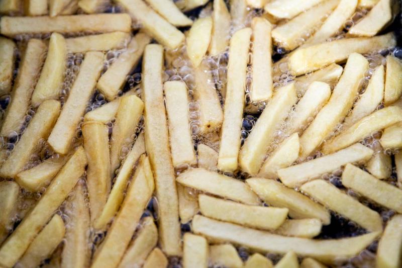 Potato slices sizzle in a fryer and become French fries.