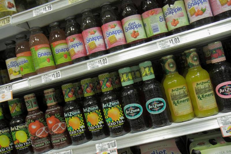 Several brands of bottled tea are on a grocery store shelf.