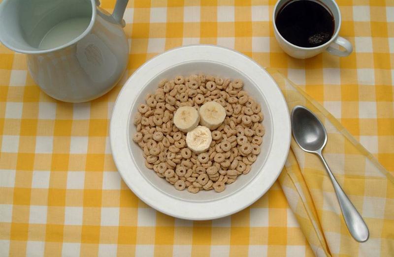 View of a table setting with a bowl of breakfast cereal (and banana slices), a cup of coffee, and a pitcher of milk