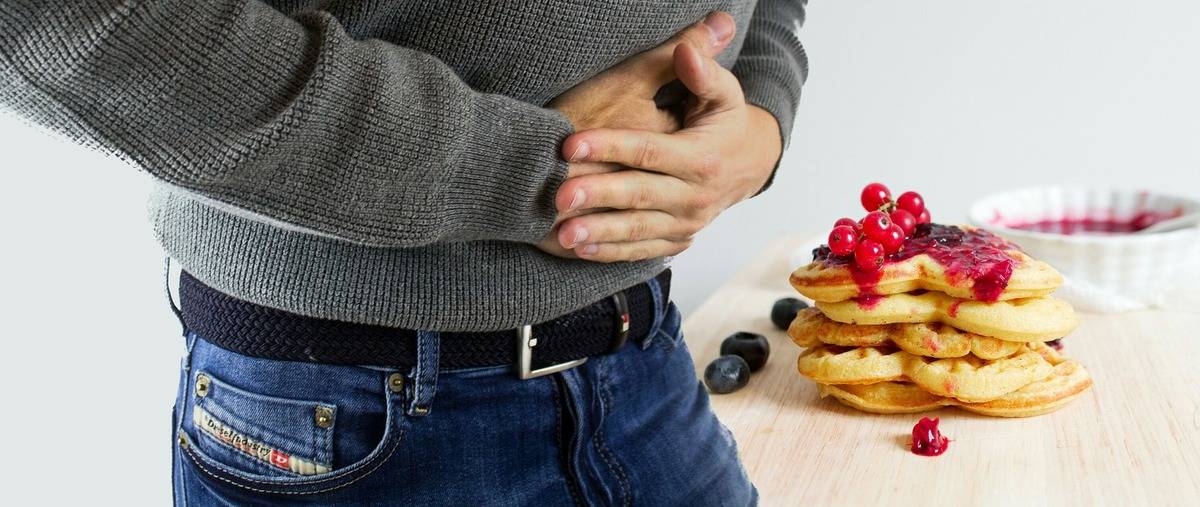 a man holding his stomach while looking at a stack of waffles