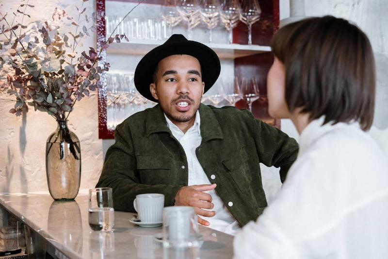 man-in-black-suit-jacket-and-black-hat-sitting-beside-table