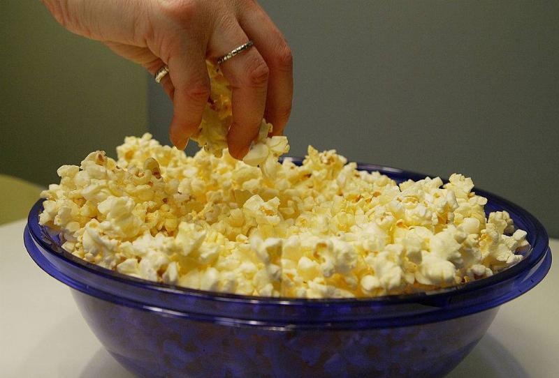 A woman grabs freshly popped microwave popcorn from a bowl