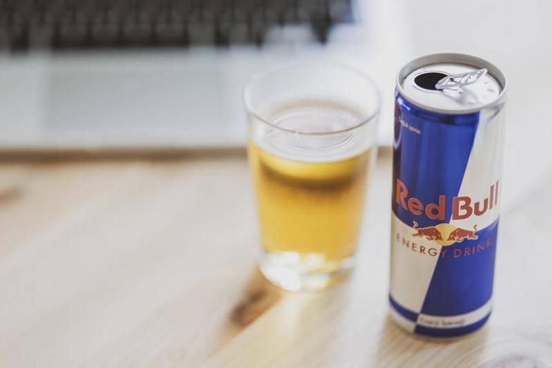 red bull Red bull is poured into a cup next to a laptop.