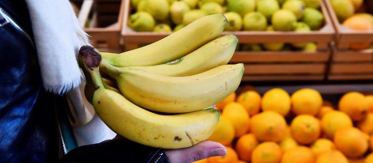 A person picks up a bunch of bananas in a store.
