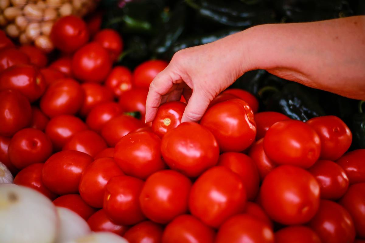 A woman selects a tomato from a pile.