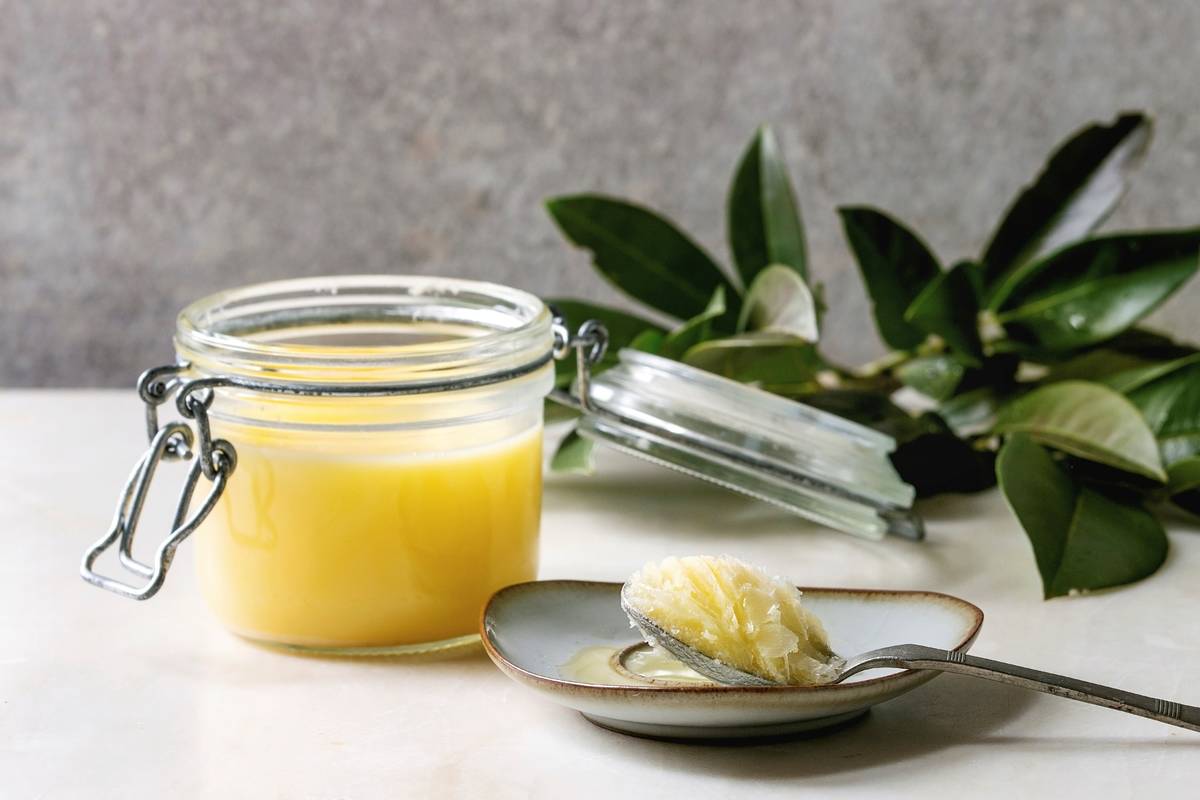 Butter is on a spoon and a glass jar.