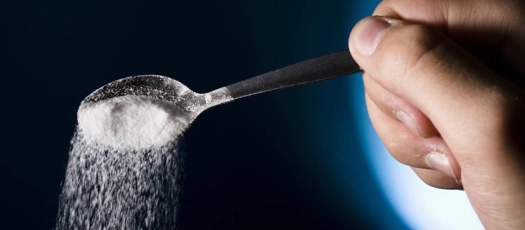 A person pours salt out of a spoon.