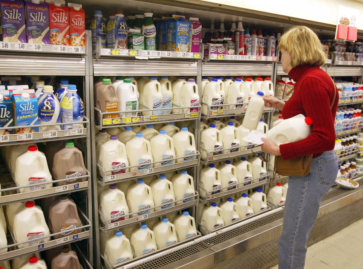 A woman chooses a milk gallon from a grocery store.