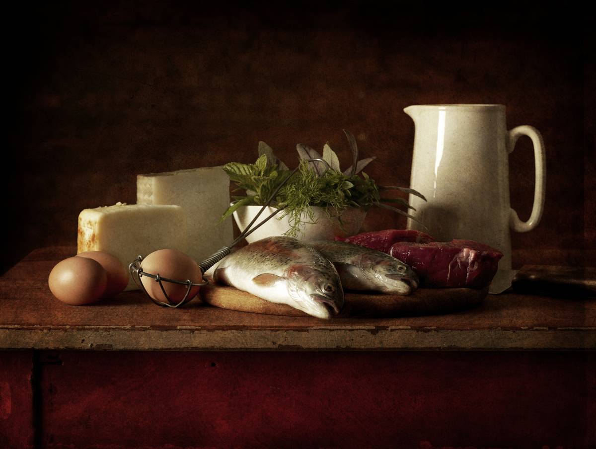 Animal products such as cheese, eggs, and fish lay on a table.