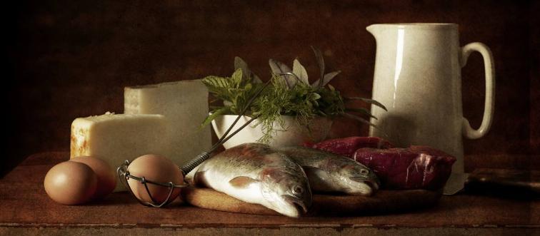 Animal products such as cheese, eggs, and fish lay on a table.