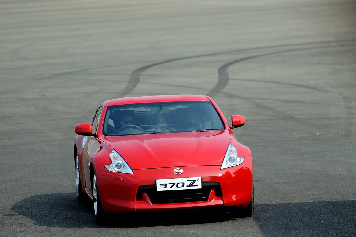 A red Nissan 370Z sports car drives across asphalt. 