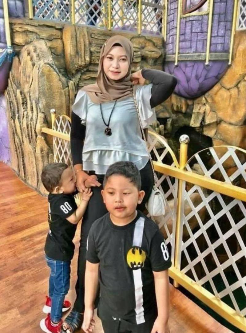 woman stands with sons—one clearly distracted and the other one biting her hand