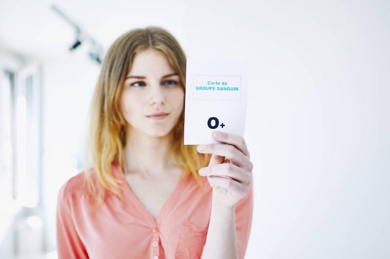 A woman holds up a card showing her blood type, O positive.