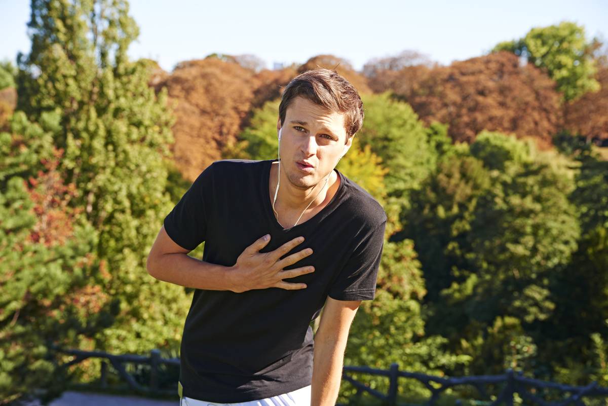 A man clutches his chest in pain while on a hike.