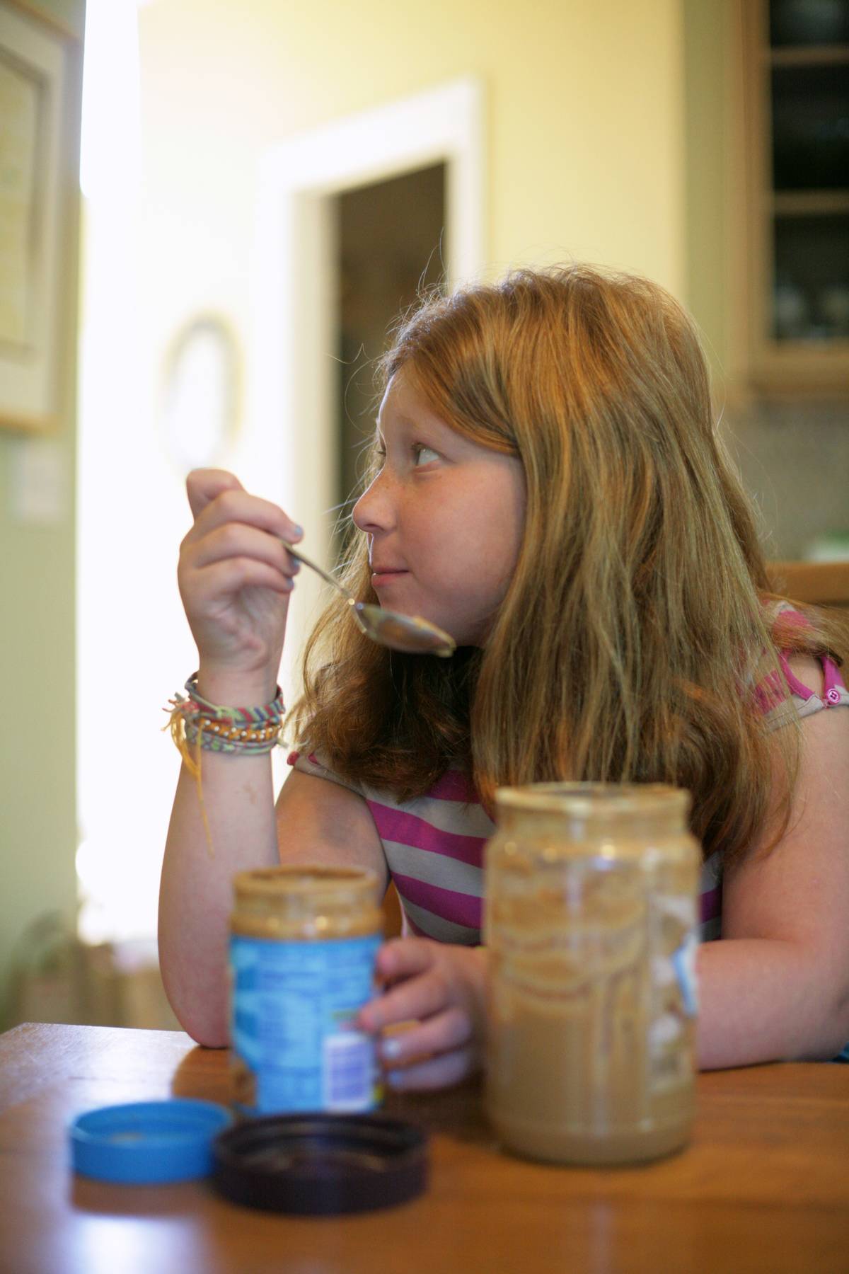 A girl eats from a jar of peanut butter.