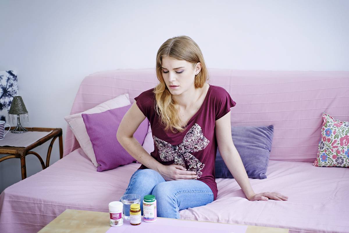 A woman on the couch clutches her stomach while looking at medication.