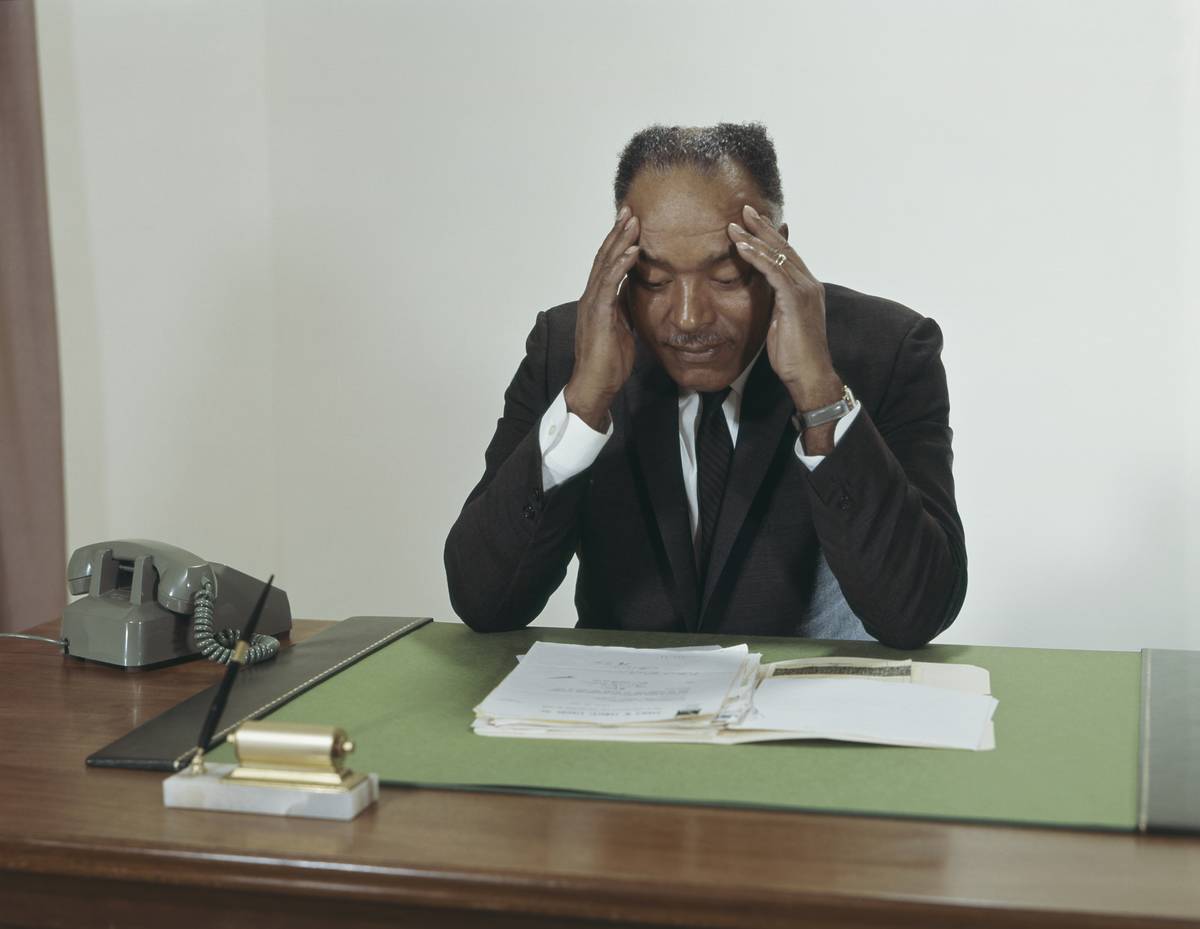 A businessman presses his fingers against his temple while sitting as his desk.