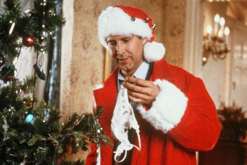 A still from Christmas Vacation shows a man dressed as santo looking at a gift.