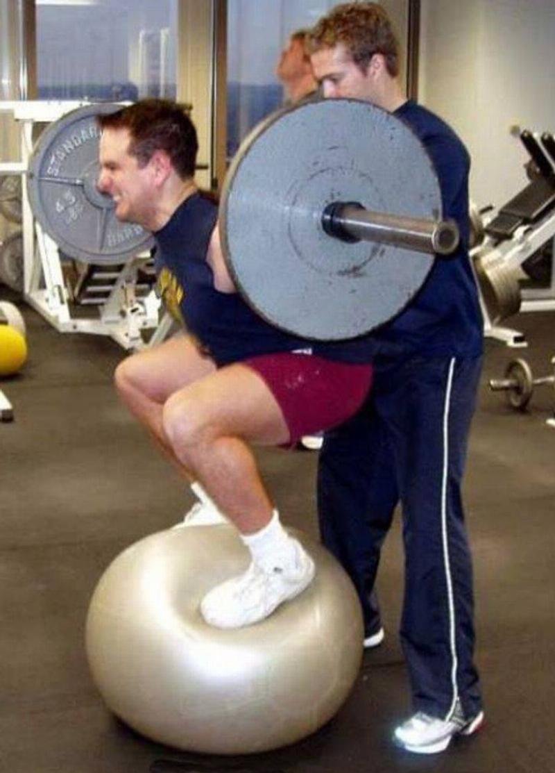 ball squats Man standing on yoga ball while lifting weights