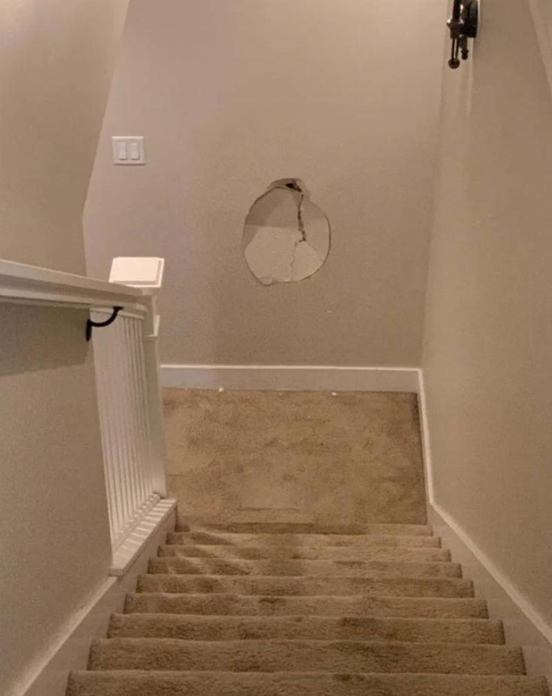 large hole in drywall at the bottom of a stairwell