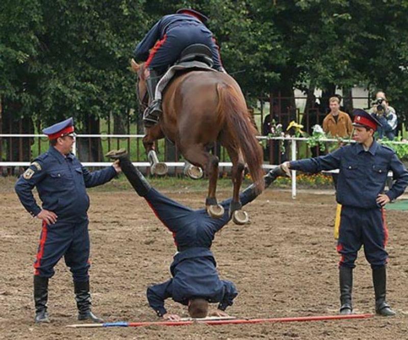 Horse jumping over a man doing the splits while upside down--it looks like the horse might hit him in the family jewels