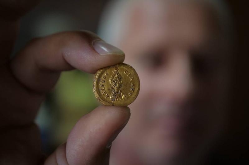 An older man holds up an ancient Roman coin.