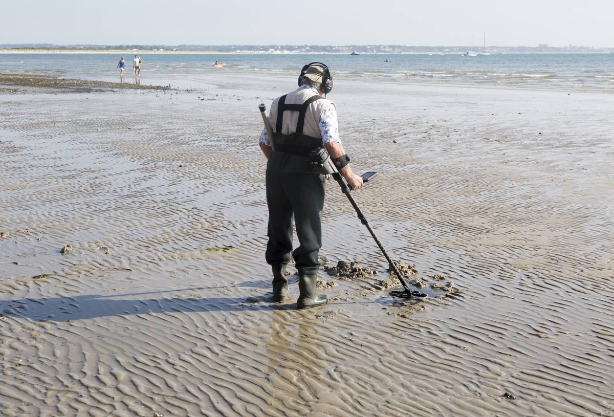 An elderly man searches the beach with his metal detector.