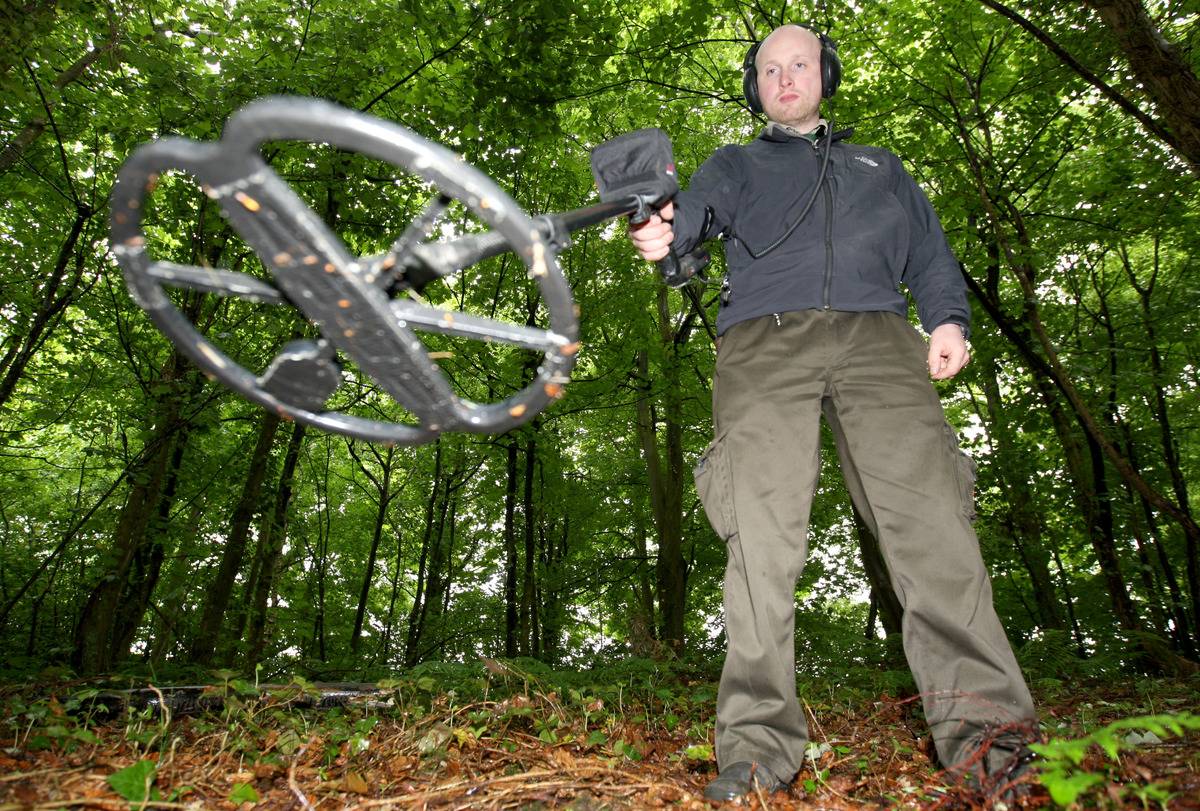 A close-up photo shows a man treasure-hunting with a metal detector.