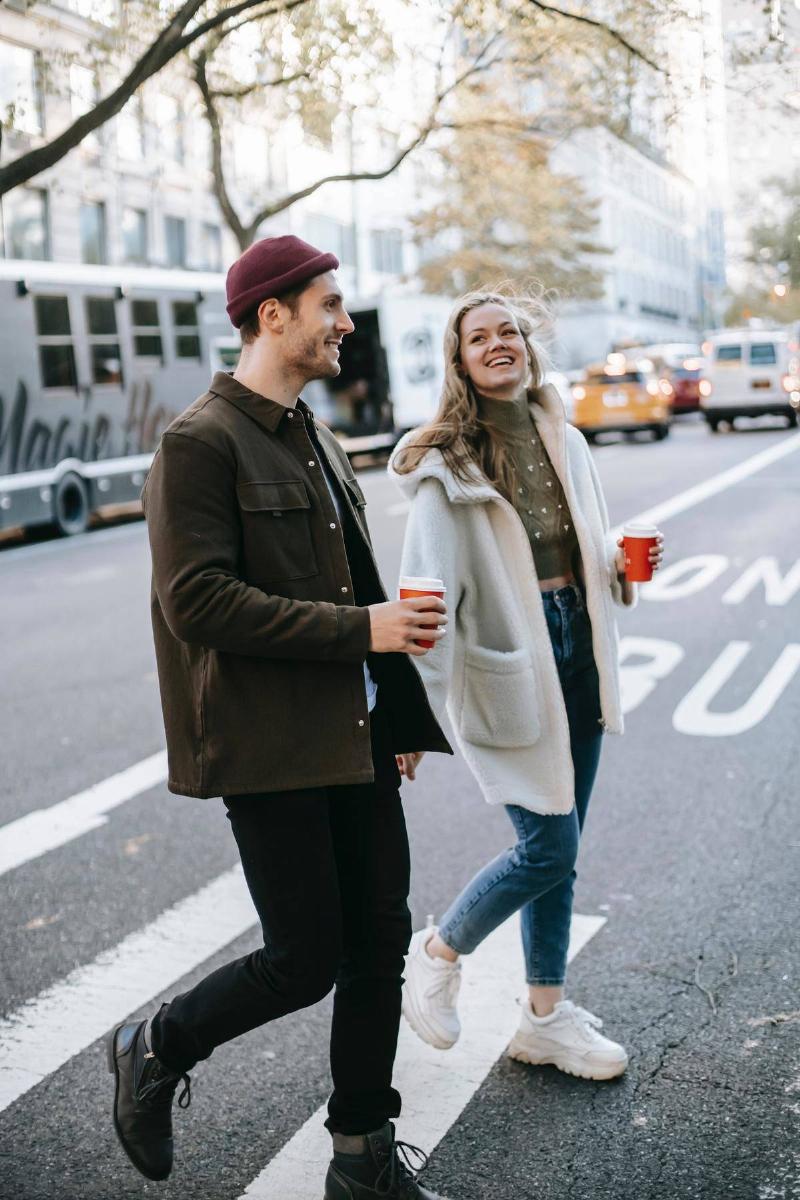 a couple walking across the street with coffee cups in their hands