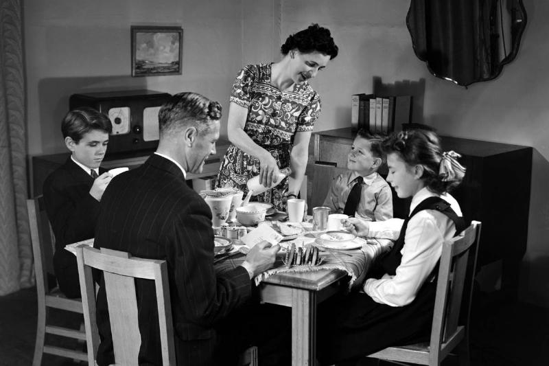 Father reads the post while mother stands to pour a drink for one of the three children. Their clothing and the radio in the background suggest a comfortable income. The family grouping of a husband, wife and two or three children appears most often in the work of Photographic Advertising Limited. The company, founded in 1926, created multi-purpose stock images with the potential for selling a range of products. Whilst enjoying its greatest success during the 1930s, it continued in business until 1977. Their trademark, the staged studio photograph resembling a film still, was its selling point and, later, its downfall.