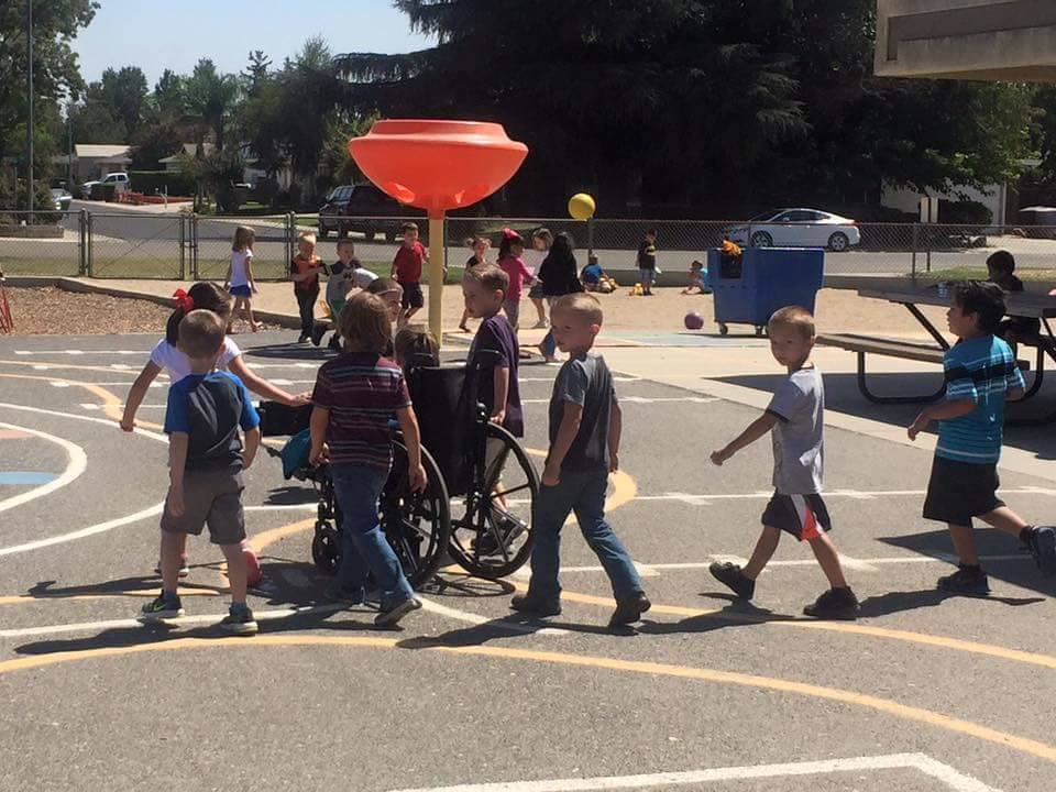 kindergarten boys pushing little girl in wheelchair
