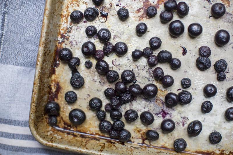 Overripe blueberries are scattered on a baking pan.