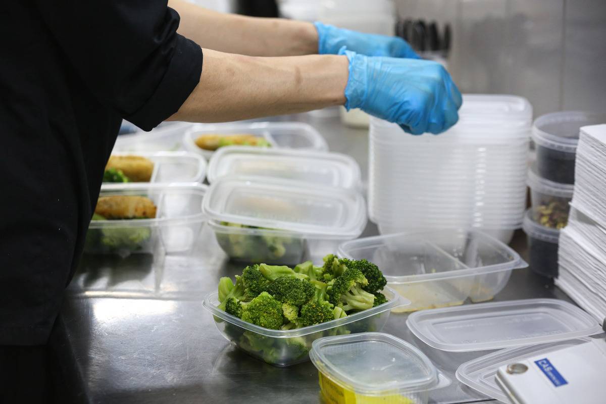 A worker wearing gloves portions broccoli into plastic containers.