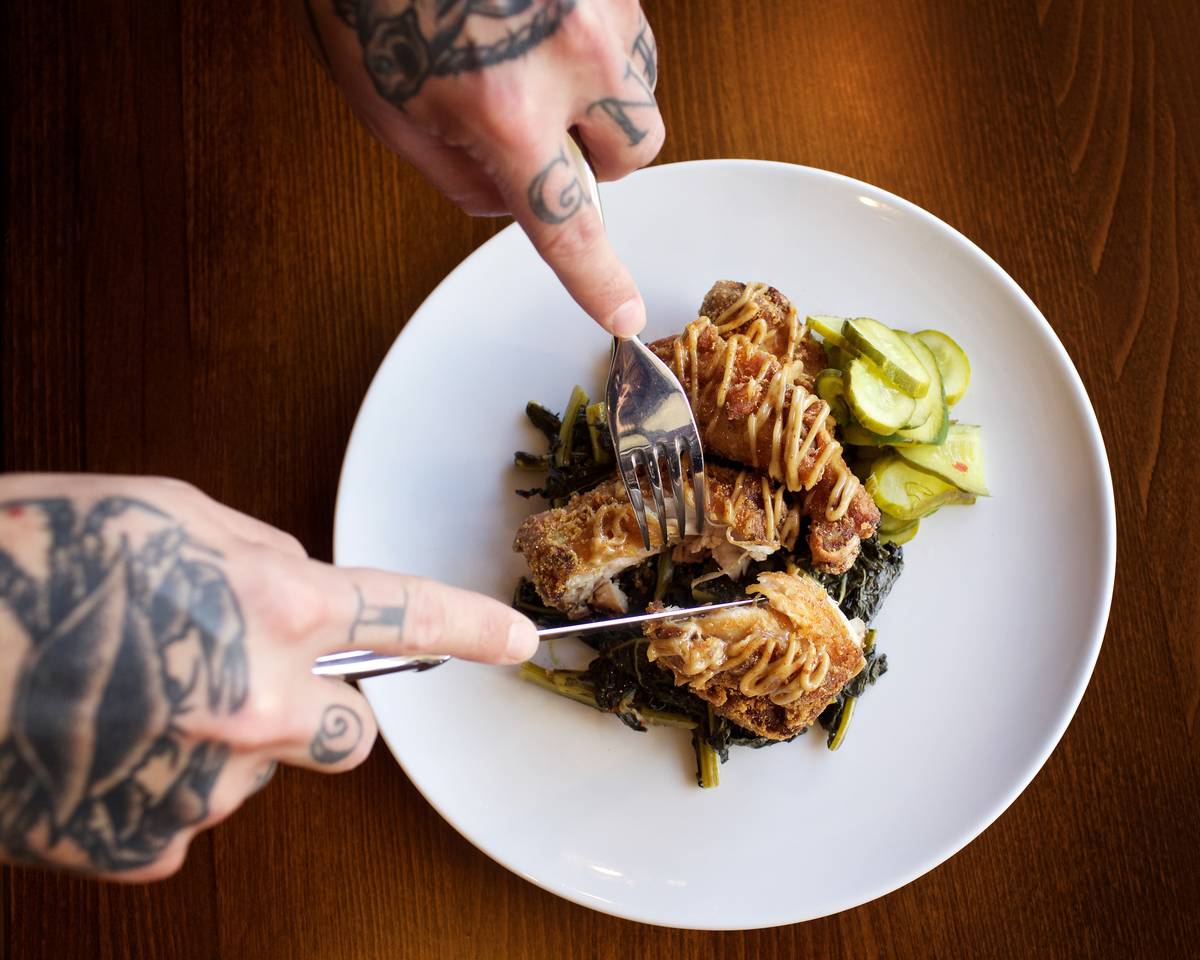 A man with tattooed hands cuts up buttermilk fried chicken.