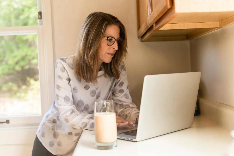 A woman works on a laptop with a glass of milk next to her.
