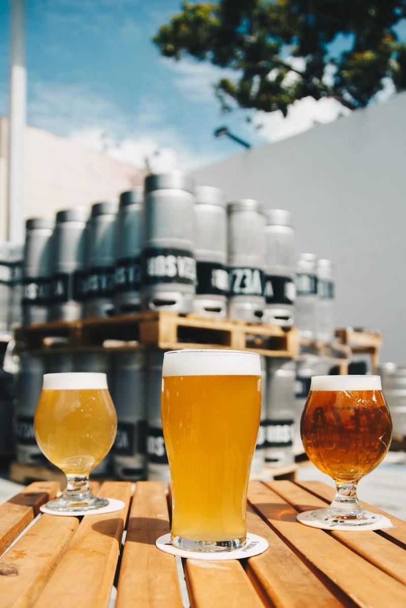 Three different beer pints at a brewery, kegs in background out of focus