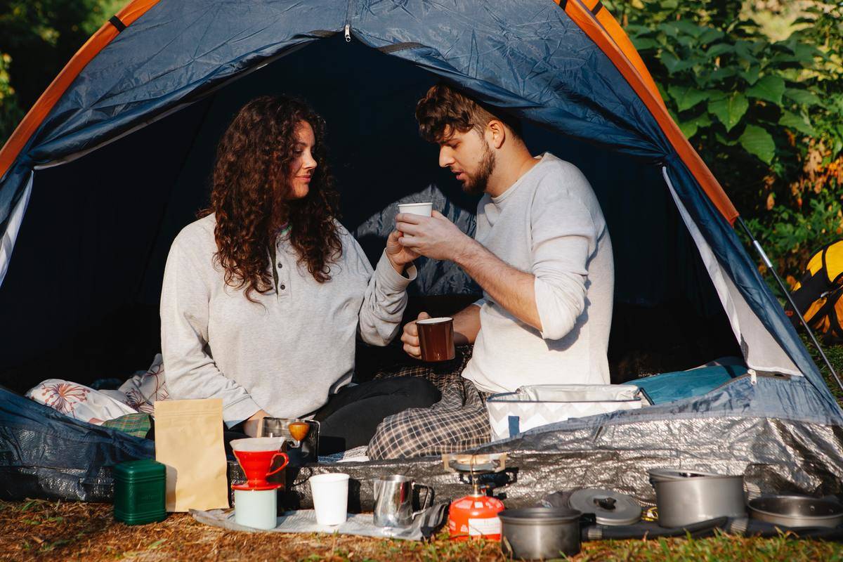 Couple drinks coffee while camping in tent