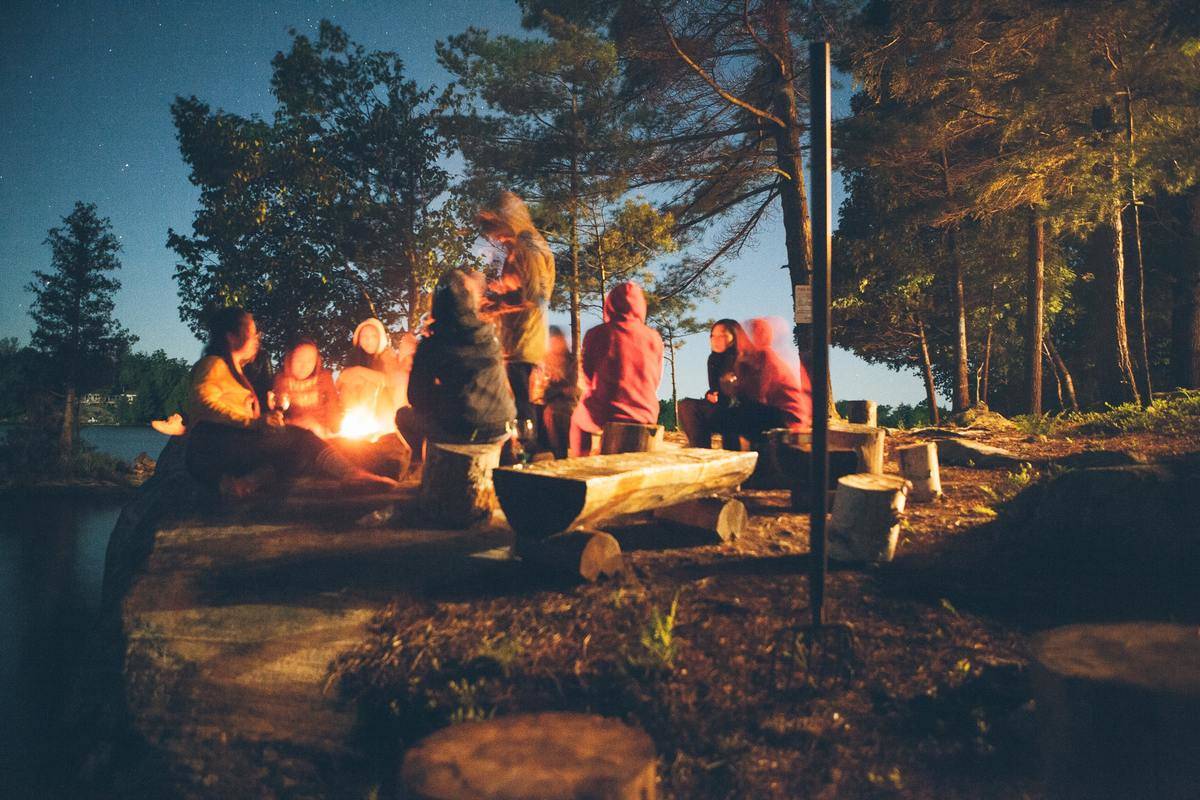 Group of people hang out on log benches around bonfire