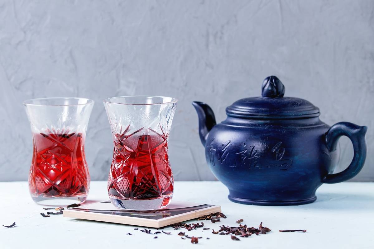 njm-drinks Two traditional asian style glasses with hibiscus tea karkade, served with dry hibiskus and dark blue ceramic teapot over blue and gray textured background
