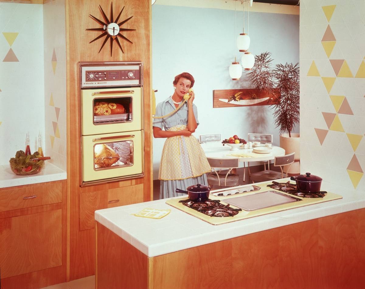 A housewife speaks on the phone in a kitchen.