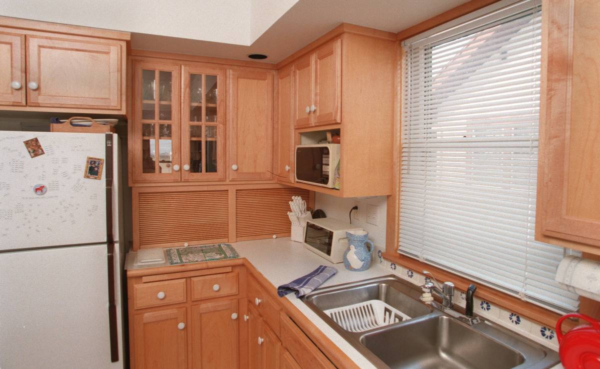A kitchen in the 1990s has cabinets of pale wood and white granite countertops.