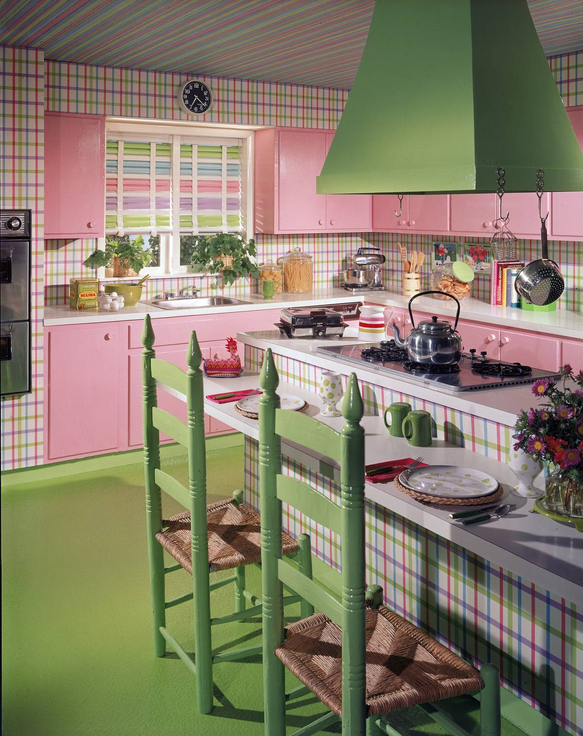 A model 1970s kitchen includes green and pink plaid wallpaper with pink cabinets, and green chairs.