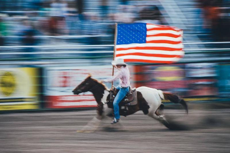 rodeo A cowboy waves an American flag while speeding around on his horse during a rodeo.