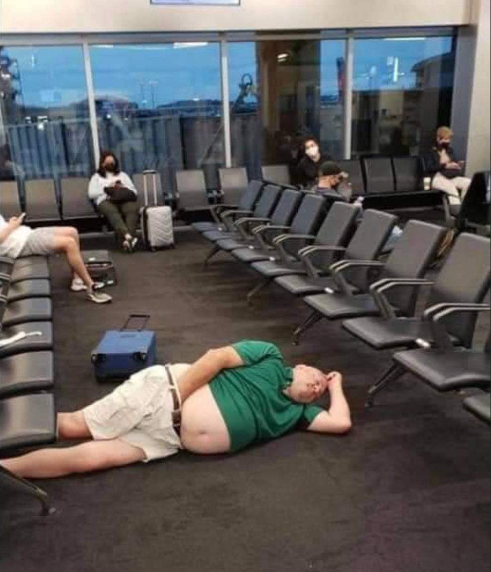 A man sleeps in the middle of an aisle at the airport.