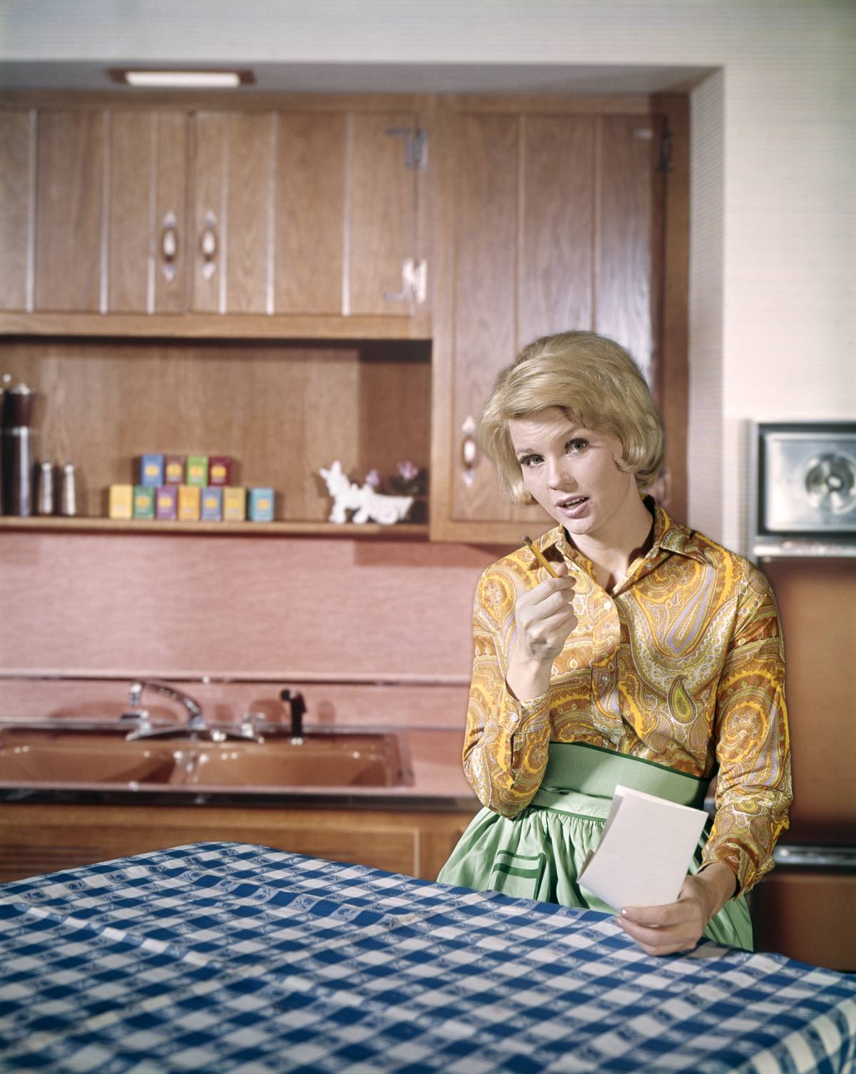 In the 1960s, a woman sits in her kitchen and thinks about a grocery list.