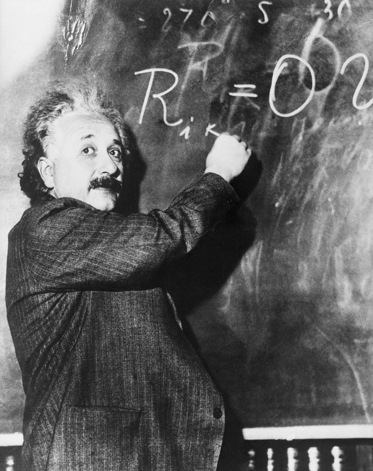 A scientists writes physics equations on a chalkboard.