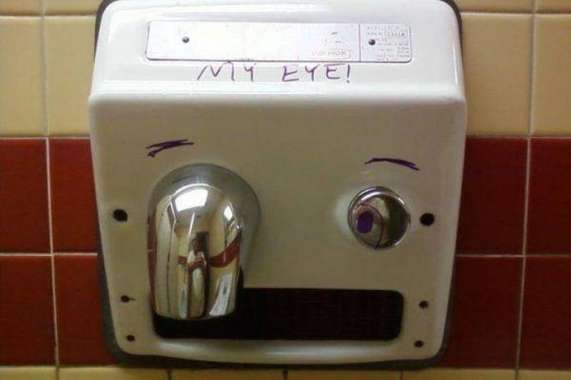Public bathroom graffiti: a hand dryer that someone has drawn eyebrows on and written 